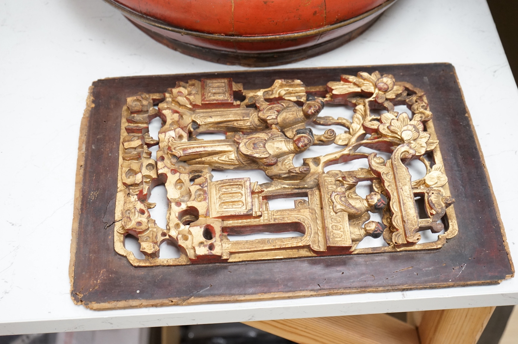A Chinese red lacquered picnic box and figurative carved gilt painted panel. Picnic box 37cm diameter. Condition - fair